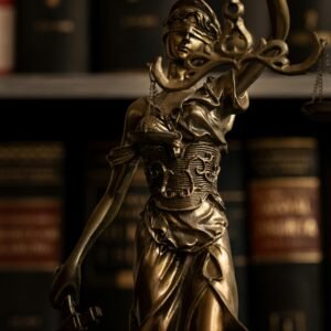 Close-up of a golden Lady Justice statue with scales in a law library setting.