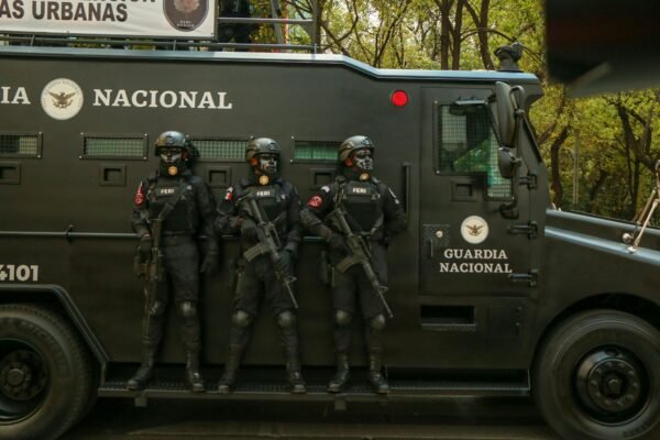 Guardia Nacional officers in tactical gear stand alert beside an armored vehicle.